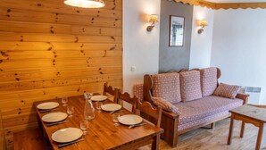 A wooden dining table set with plates and glasses, a wooden bench, and a patterned sofa against a wooden wall with a framed welcome sign. - 40m from ski slopes, 2nd floor, fitness, swimming pool, sauna, balcony, tv, ski locker, 37m² (Les Orres)