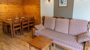 A cozy room with a wooden wall, a sofa with patterned cushions, a wooden dining table with chairs, and two wall-mounted lamps. - 40m from ski slopes, 2nd floor, fitness, swimming pool, sauna, balcony, tv, ski locker, 37m² (Les Orres)