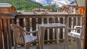 A wooden balcony with two chairs and a table, overlooking a mountain and a village. - 40m from ski slopes, 2nd floor, fitness, swimming pool, sauna, balcony, tv, ski locker, 37m² (Les Orres)