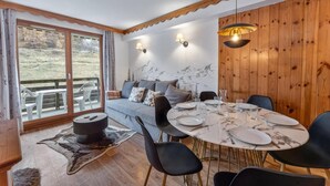 A dining area with a round table set for four, a sofa with cushions, and a view of a mountainous landscape through large windows.