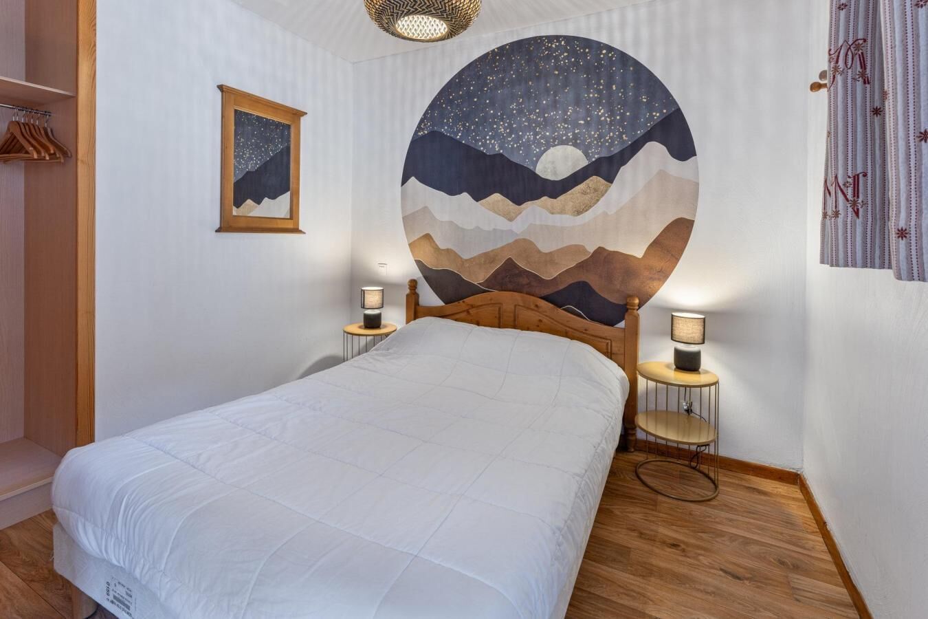 Un dormitorio con una cama, un mural del cielo nocturno en la pared, una mesita de noche con una lámpara y un cabecero de madera.