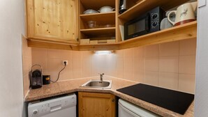 A compact kitchen with wooden cabinets, a microwave, a kettle, and a dishwasher.