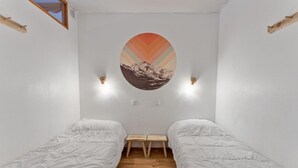A small, clean room with two single beds, a wooden bench, and a wall-mounted artwork.