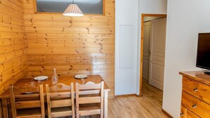 Una stanza con rivestimento in legno, un tavolo da pranzo apparecchiato per due persone, una lampada a sospensione e un televisore su un mobile in legno.