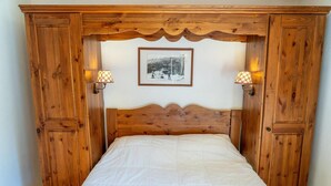Un letto con struttura in legno e copripiumino bianco imbottito, affiancato da due lampade a parete, e una fotografia in bianco e nero incorniciata appesa al muro.