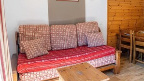 Een gezellige kamer met een gestreept bankje, een houten salontafel en een houten eettafel.
