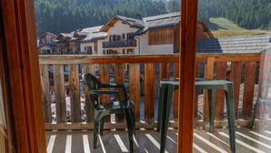 Un balcone con ringhiere in legno, due sedie di plastica verde e un tavolino.