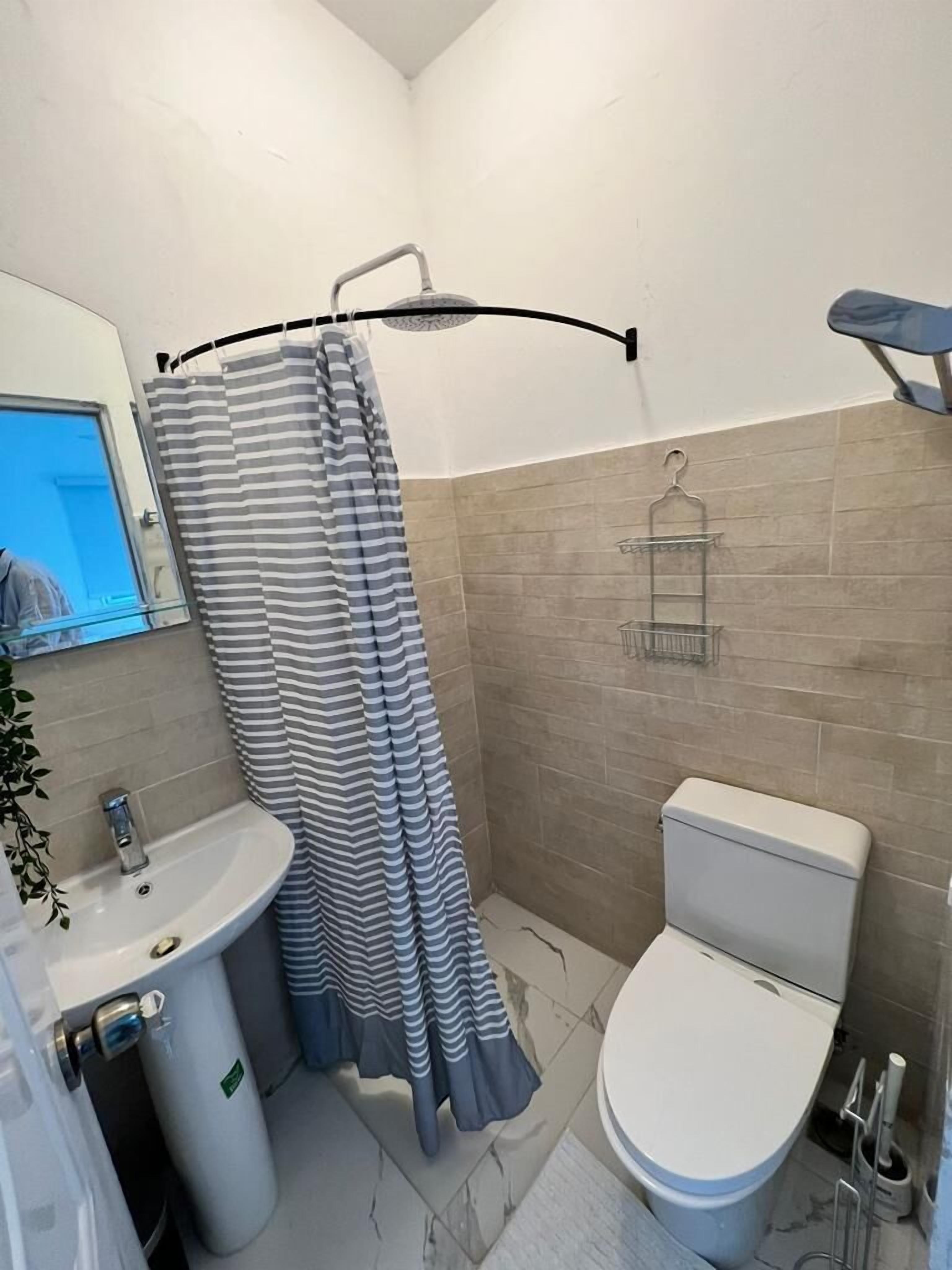 Et badeværelse med bruser, toilet, håndvask og spejl.