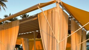 Area relax in spiaggia con poltrone imbottite e un tavolo, coperta da un tendale giallo.
