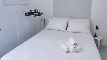 Cama bem arrumada com lençóis e toalhas brancas, luminária de cabeceira e ar-condicionado fixado na parede.