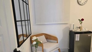 Una stanza piccola e pulita con un divano, un tavolino con un vaso, una sveglia e un frigorifero.
