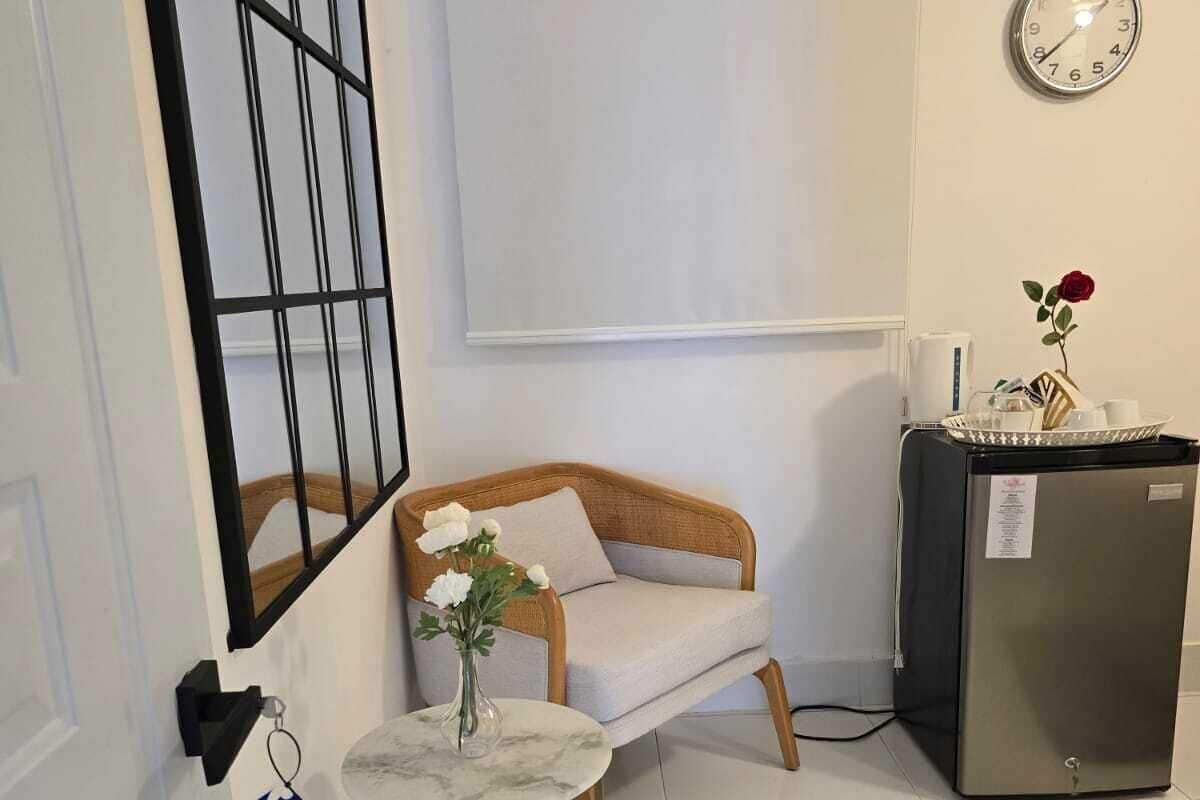 Una habitación pequeña y limpia con un sofá, una mesa pequeña con un jarrón, un reloj y un refrigerador.