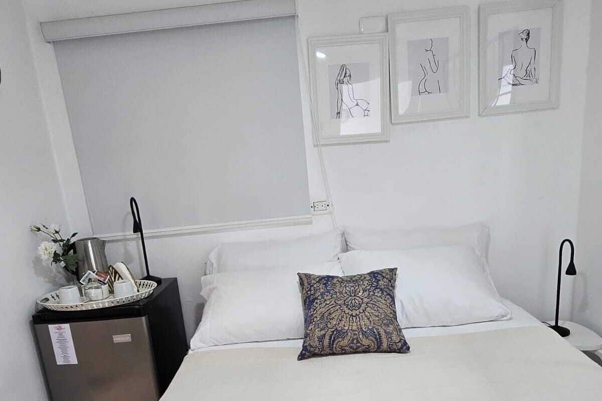 Una habitación de hotel con una cama, una mesita con lámpara y un cubo de basura.