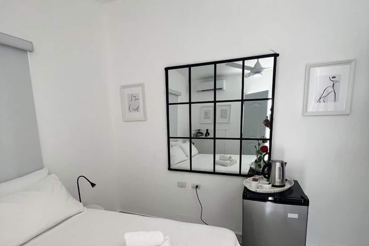 Una habitación de hotel minimalista con una cama grande, una kitchenette pequeña y un ventilador de techo.