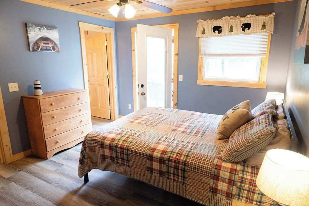 Un dormitorio con colcha escocesa, cómoda de madera y ventana con adornos.