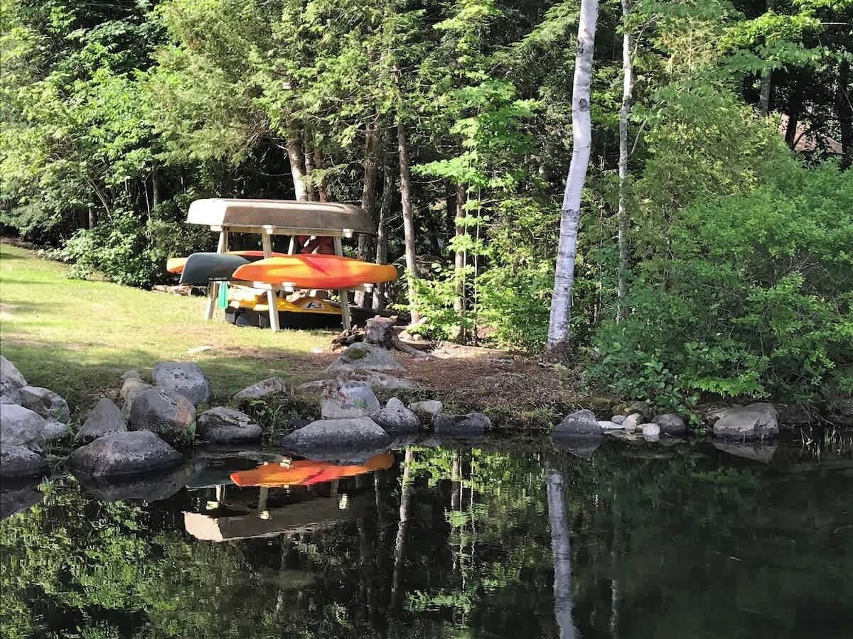 A campsite with a tent and a canoe by a calm lake surrounded by trees.