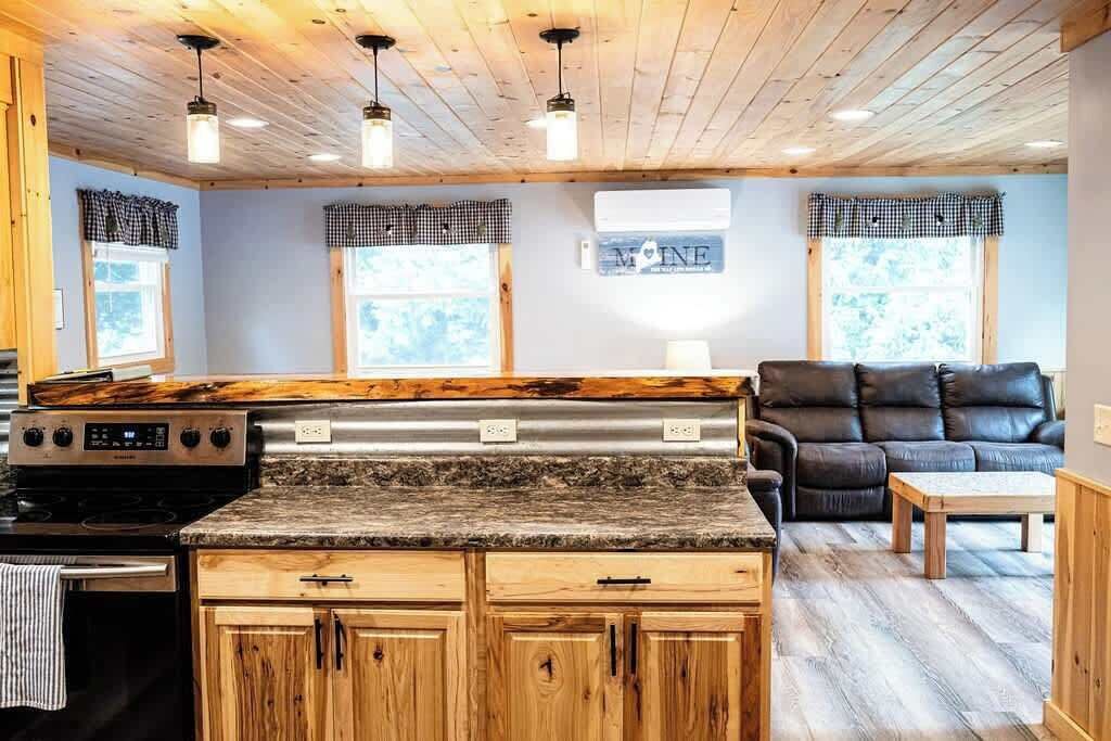 A kitchen with wooden cabinets, a granite countertop, a black stove, and a black leather couch in the living area.