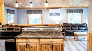A kitchen with wooden cabinets, a granite countertop, a black stove, and a black leather couch in the living area. - Four-Season Getaway on Upper Cold Stream Pond (Lincoln)