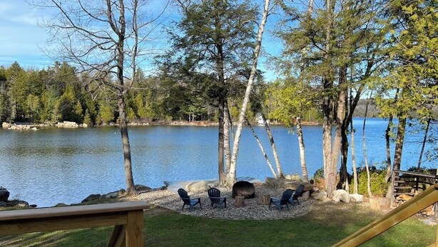 A wooden deck overlooking a lake with trees and a fire pit area. - Four-Season Getaway on Upper Cold Stream Pond (Lincoln)