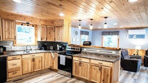 A kitchen with wooden cabinets, a central island, and a dining area with a couch. - Four-Season Getaway on Upper Cold Stream Pond (Lincoln)