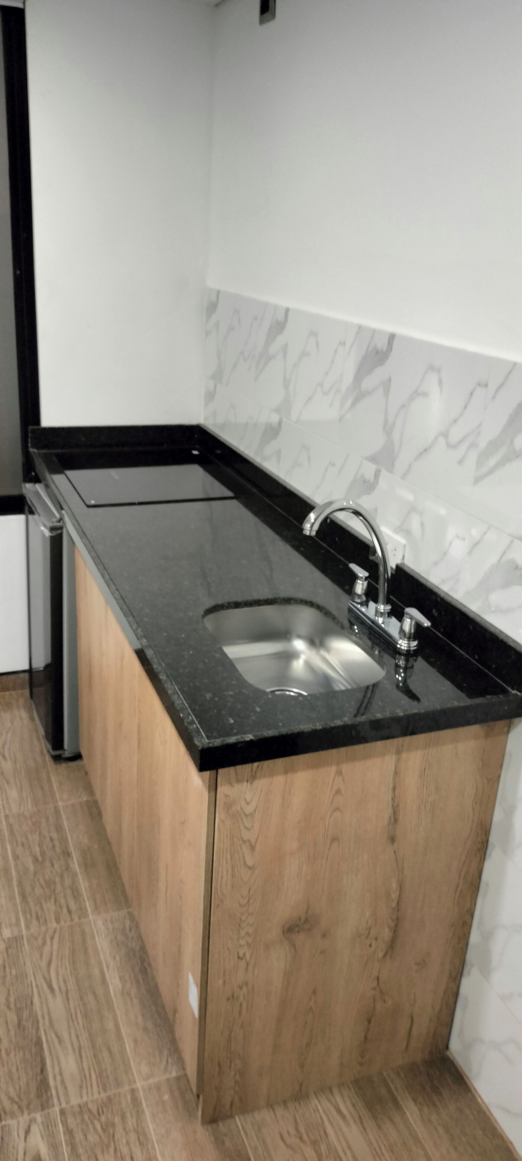 Una cocina con encimera negra, pileta de acero inoxidable y muebles de madera.