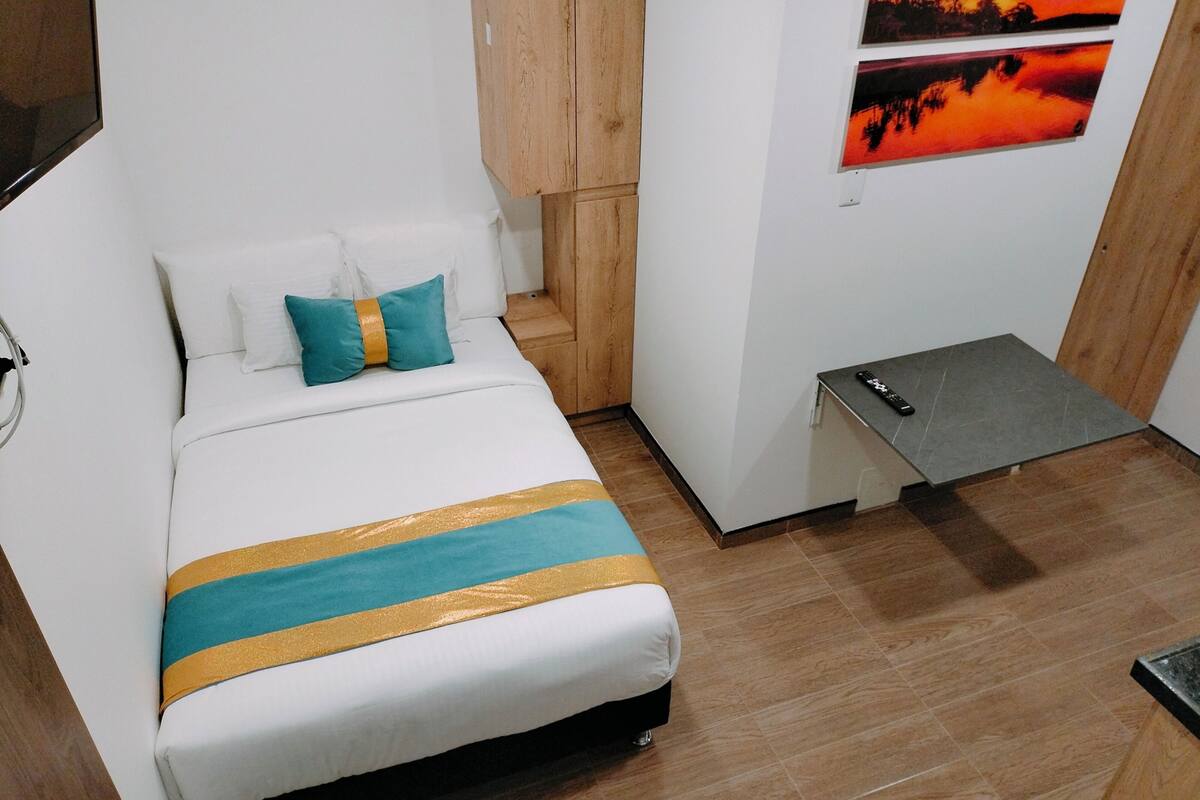 Een knus, netjes ingerichte slaapkamer met een bed, nachtkastje en een tv aan de muur.