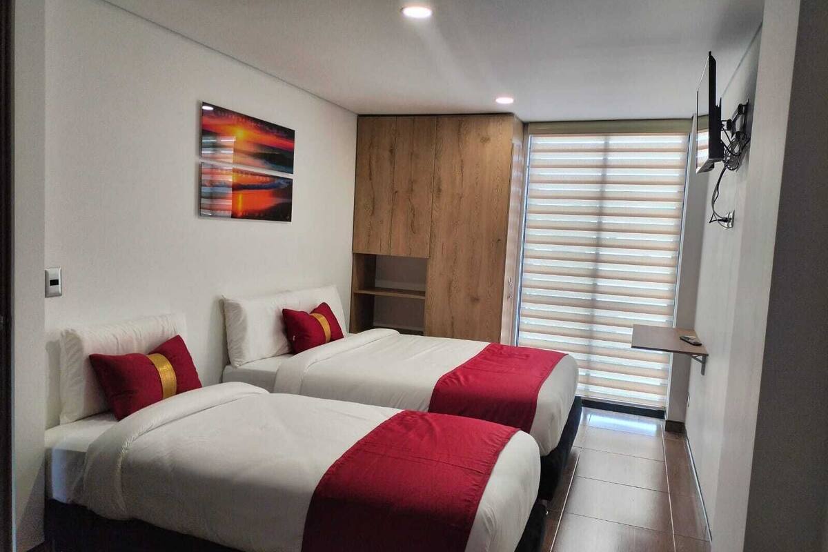 Een hotelkamer met twee bedden, een houten kast, een schilderij en een raam met jaloezieën.