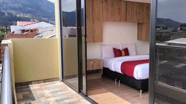 Ein Schlafzimmer mit einem Bett, einem Holz-Kopfteil, einem Nachttisch und Blick auf die Stadt durch große Fenster.