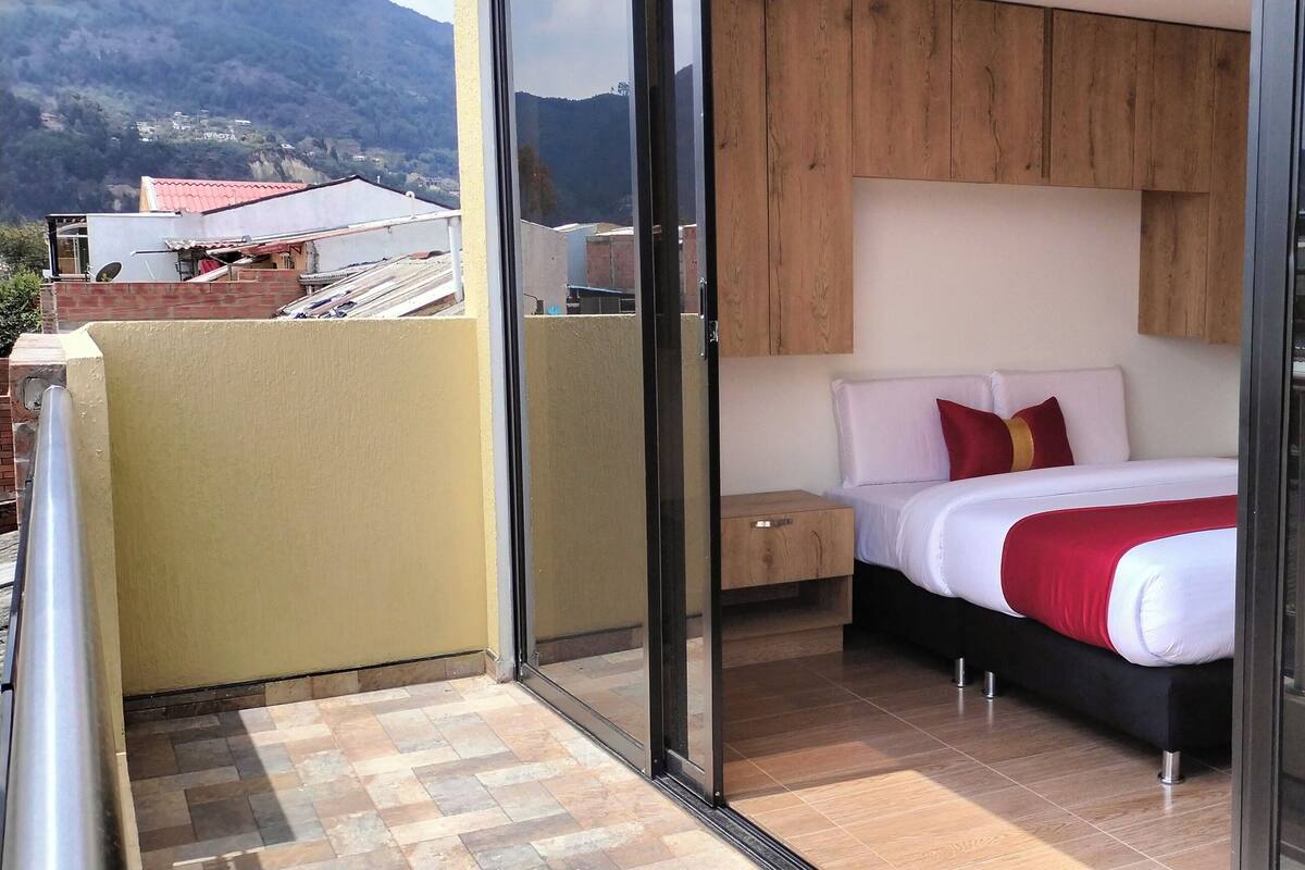 Een slaapkamer met een bed, een houten hoofdbord, een nachtkastje en uitzicht op de stad door grote ramen.