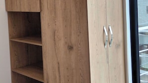 Ein Zimmer mit großem Holzschrank, Glastür zum Verschieben und einer rotfarbenen Bettdecke.