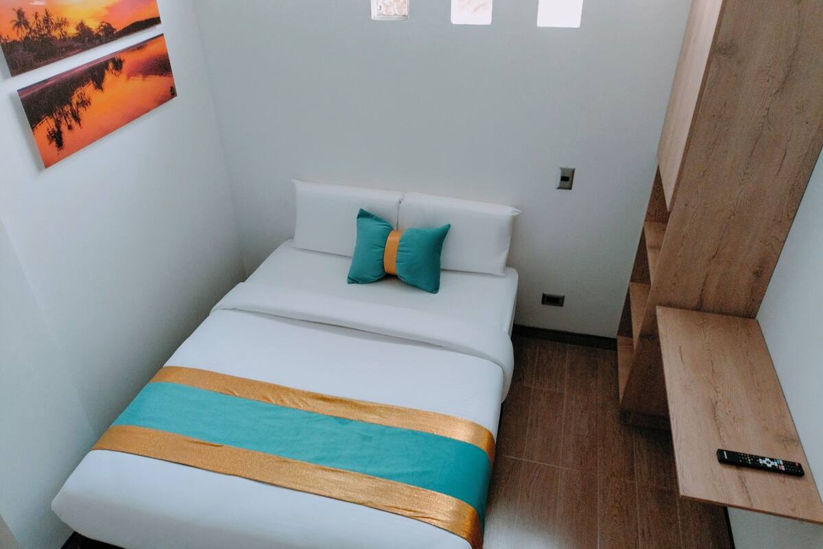 Een compacte, verzorgde slaapkamer met een enkel bed, een nachtkastje en een wandplank.