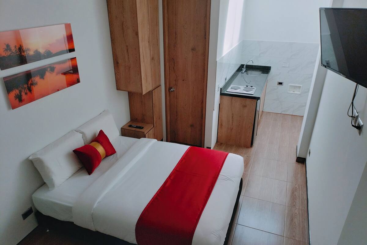 Een kleine hotelkamer met een bed, een houten garderobe, een kitchenette en een televisie.