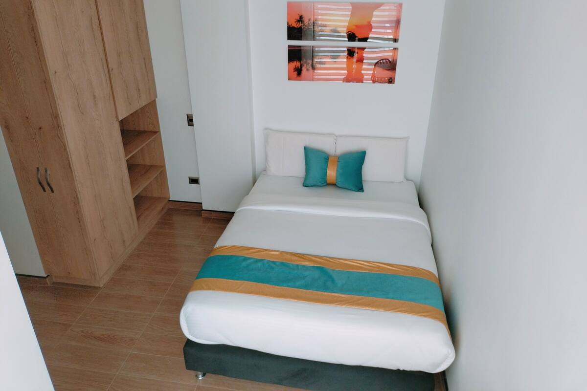 Een slaapkamer met een bed, een houten garderobe, een witte muur en een lijst met een afbeelding.