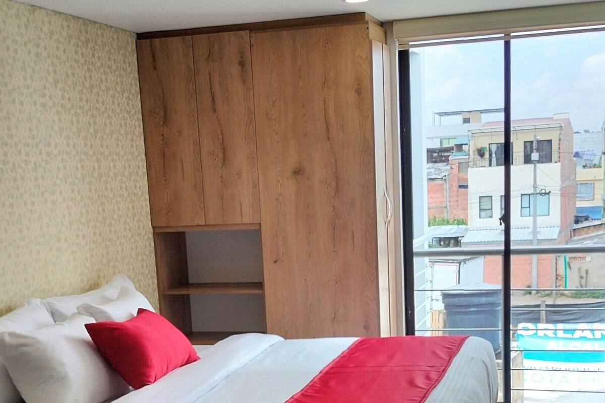 Een hotelkamer met een bed, een wand van houten panelen, een raam met uitzicht op gebouwen en een betegelde vloer.