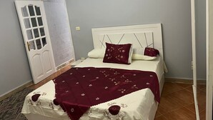 A bedroom with a white bed, a patterned throw blanket, and a red pillow. - Beit Baitk 1 (6th of October City)