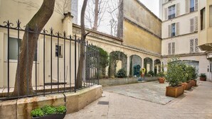 Un patio con cerca de hierro forjado, plantas en macetas y un edificio con ventanas arqueadas.