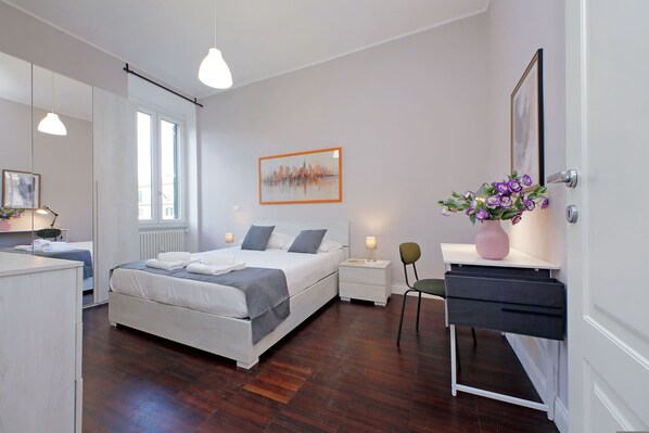 A modern bedroom with a large bed, bedside tables, a desk, and a chair.