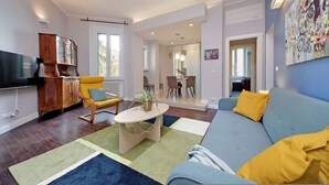 A modern living room with a sofa, armchair, and a wooden cabinet. - 4bnb - Armot House Vatican Apartment (Rome)