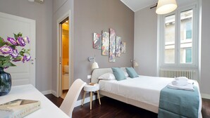 A bedroom with a bed, bedside table, lamp, artwork on the wall, and a window. - 4bnb - Armot House Vatican Apartment (Rome)