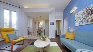 A modern living room with a yellow rocking chair, a blue sofa, and a round coffee table with a plant. - 4bnb - Armot House Vatican Apartment (Rome)