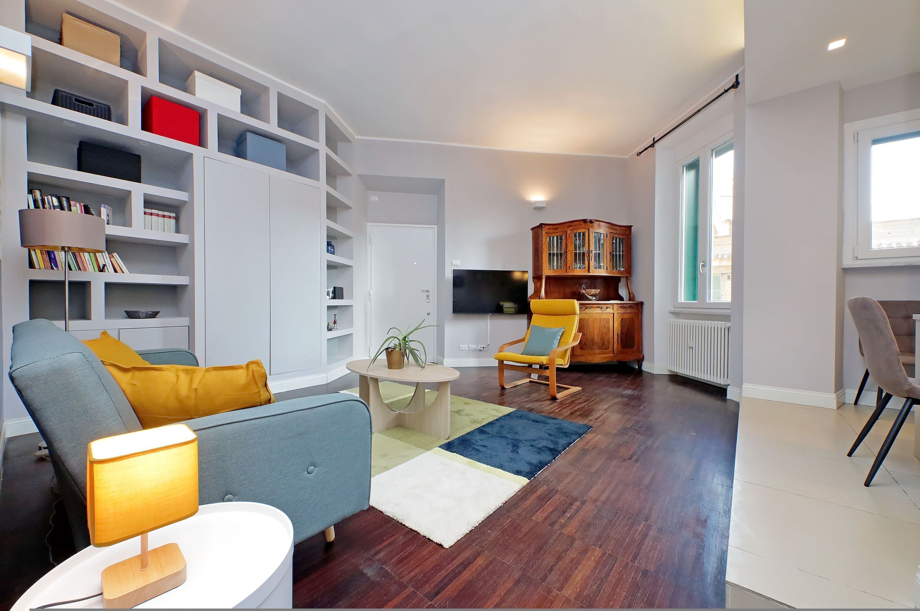 A modern living room with a sofa, armchairs, a coffee table, a bookshelf, and a television.