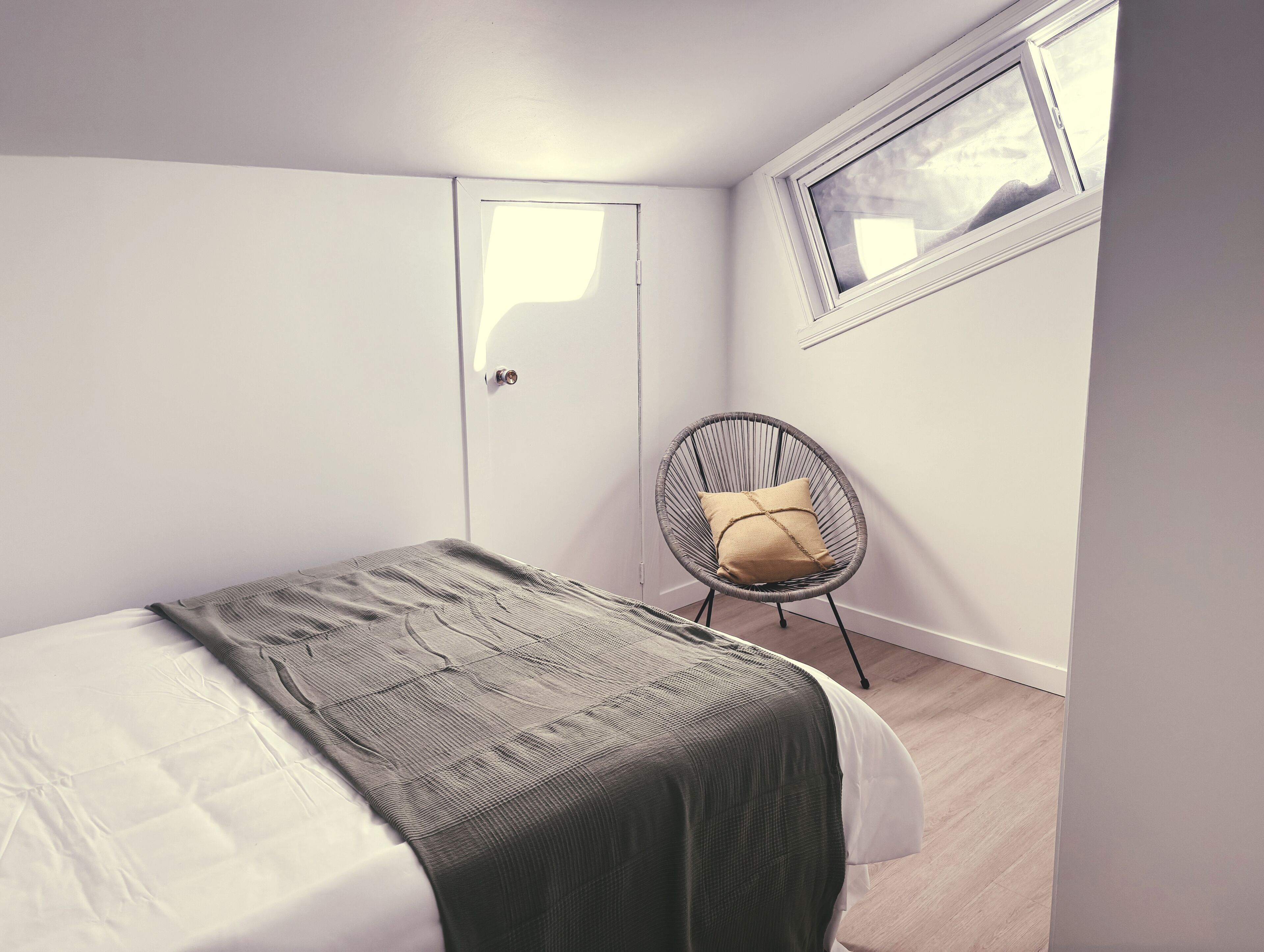 Een slaapkamer met een bed, een stoel, een raam en een deur.