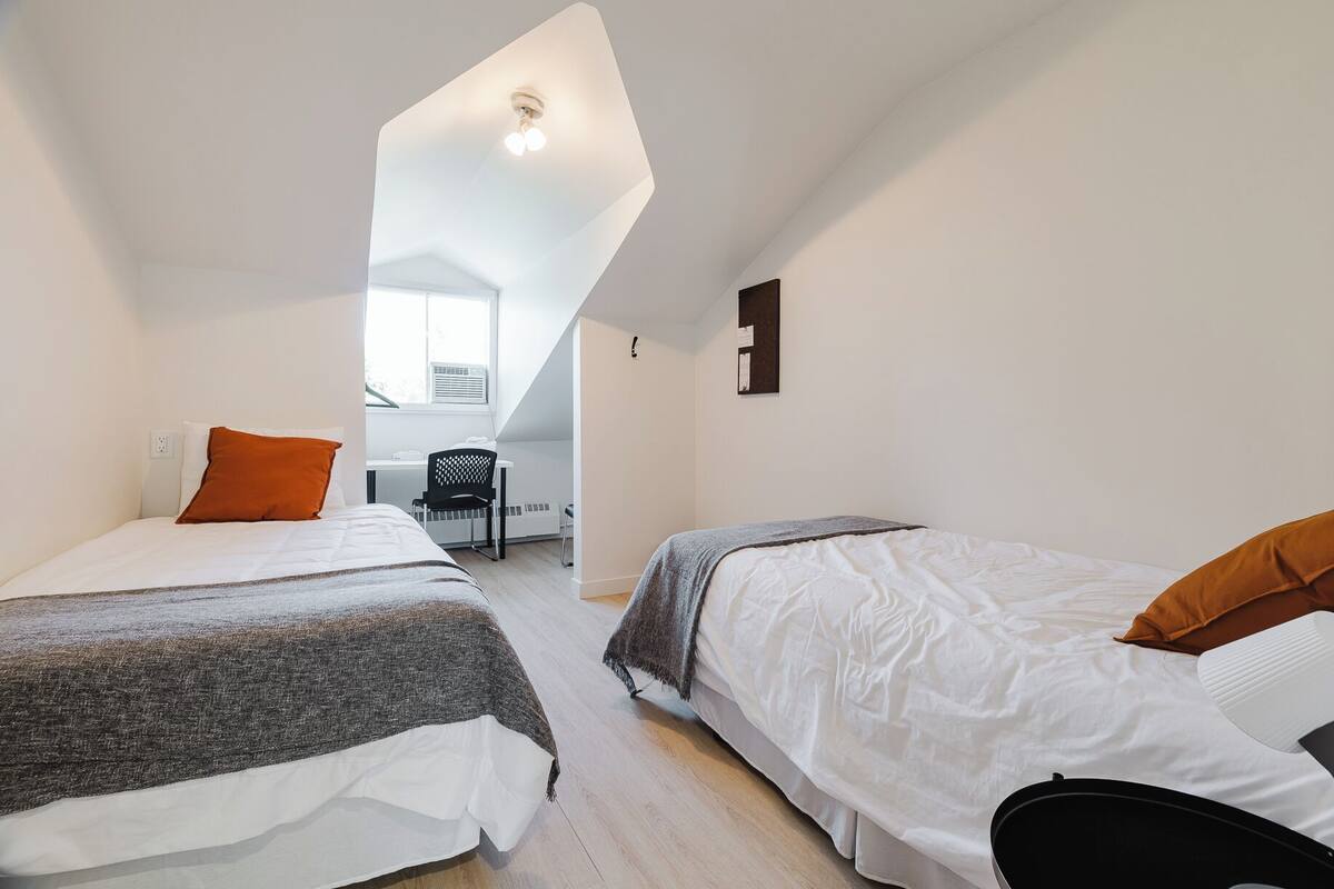 A compact, well-lit room with two beds, a desk, and a chair.