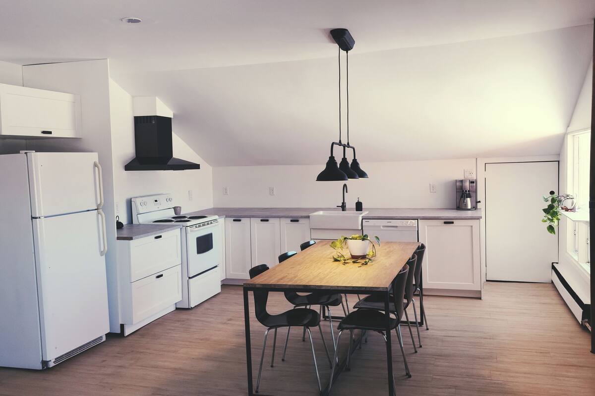 A modern kitchen with white appliances, a wooden dining table, and black chairs.