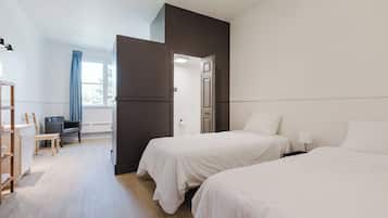 A hotel room with two beds, a desk, a chair, and a wardrobe.