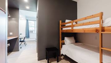Una camera con letto a castello, una scrivania, una sedia, uno sgabello e una finestra con tende.