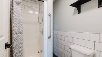 A bathroom with a shower, toilet, and a white tiled wall.