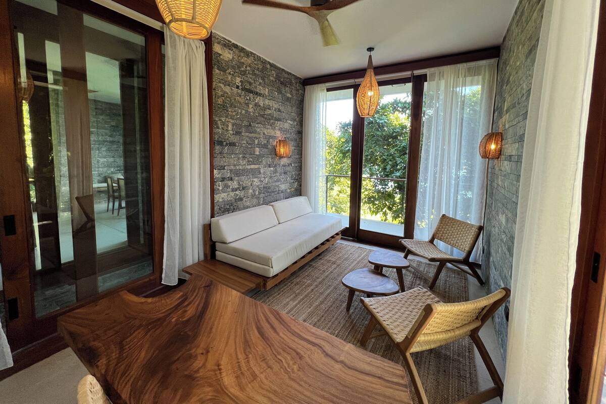 A modern interior with a wooden dining table, a sofa, wicker chairs, and a stone wall.