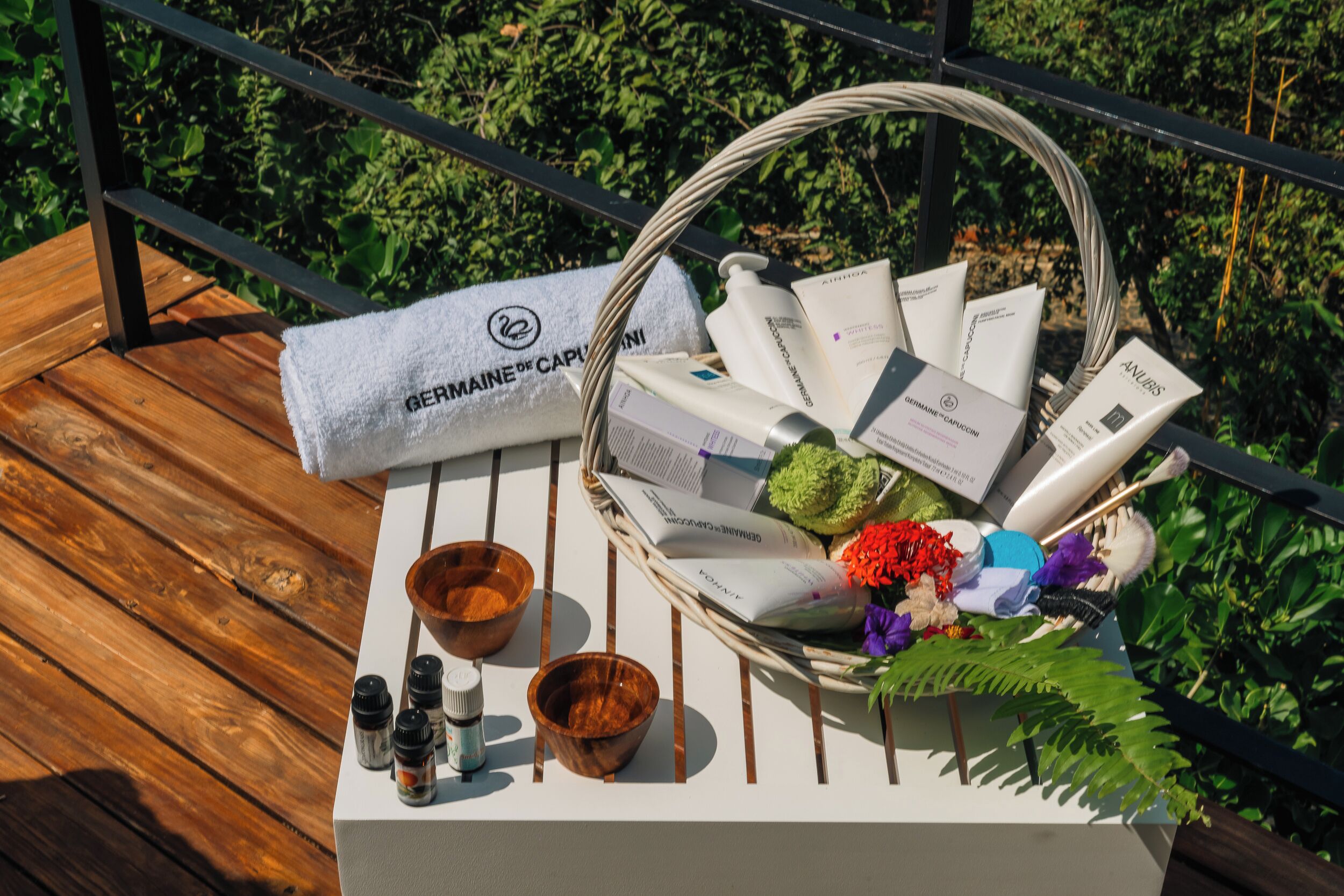 A wooden deck with a towel, a basket of toiletries, and a wooden bowl.