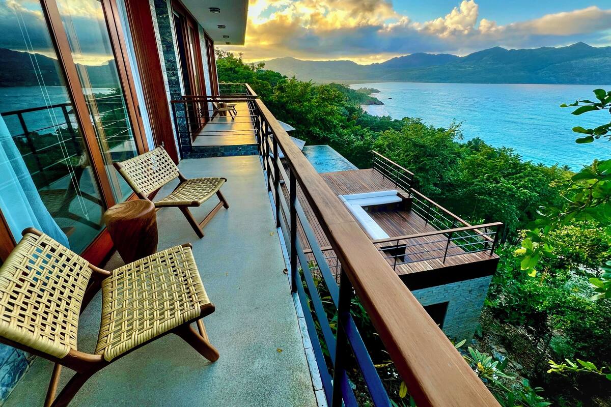 A balcony with wicker chairs, a wooden deck, and a view of a lake and mountains.